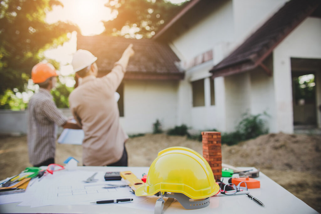 A yellow hardhat with two new home builders pointing at an El Paso home in the background.